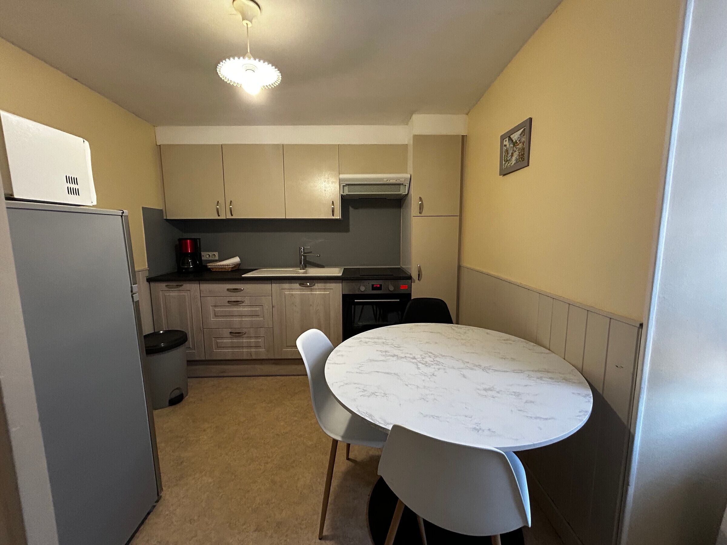 A compact kitchen with a refrigerator, stove, sink, and a dining table with chairs.