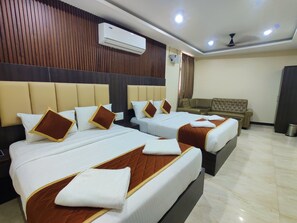 A hotel room with two beds, a sofa, an air conditioning unit, and a ceiling fan.