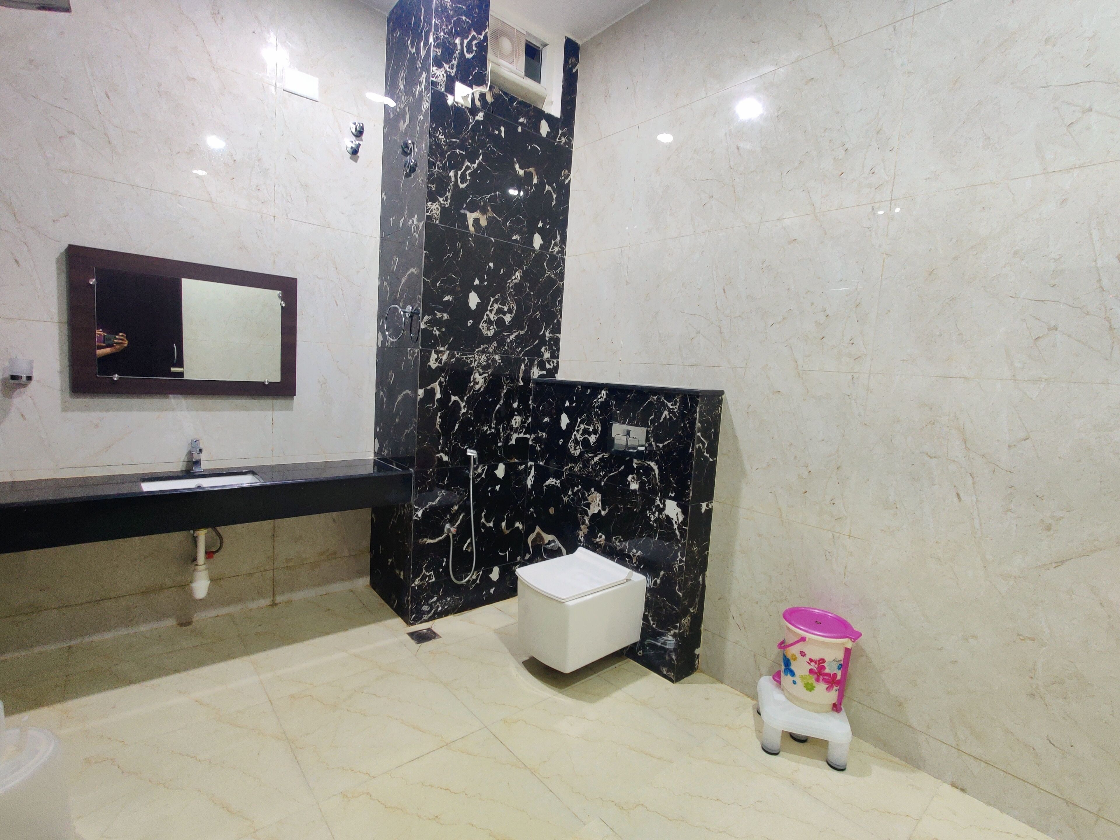 Une salle de bain avec un lavabo en marbre noir, des toilettes blanches et une petite poubelle rose.