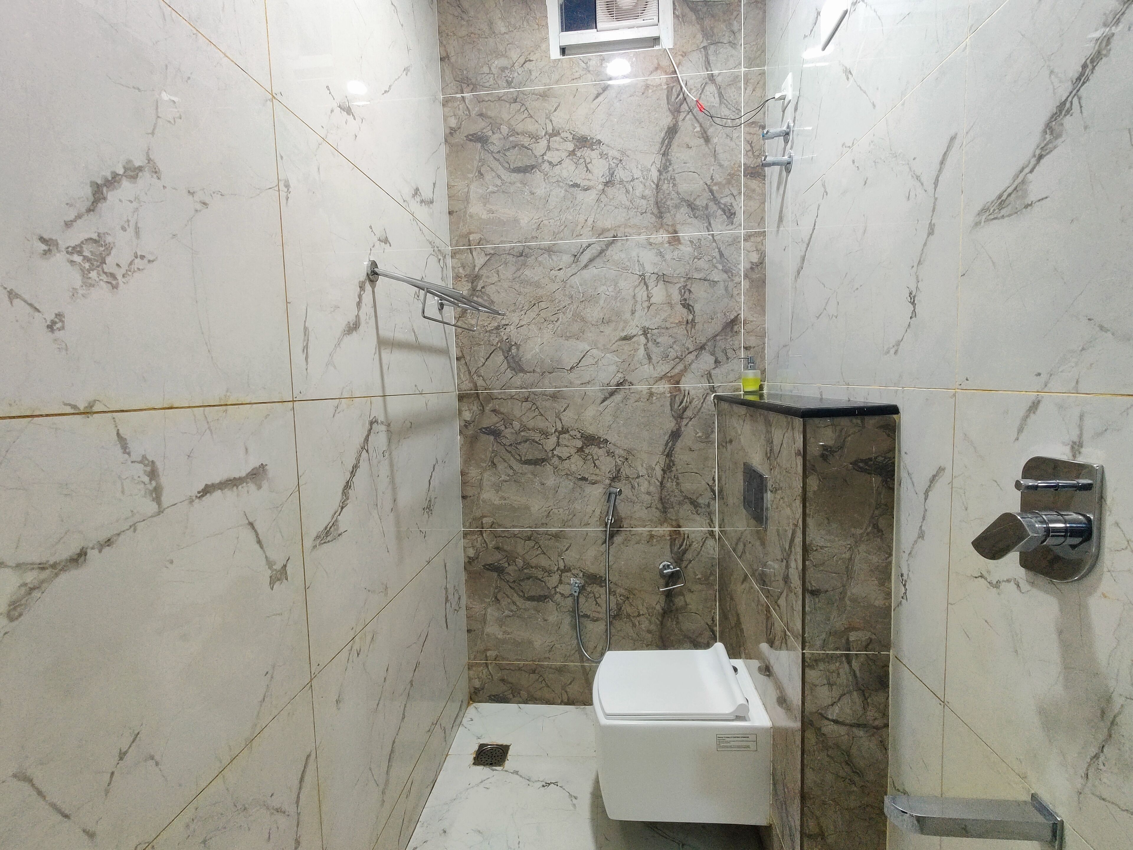 Un baño con paredes de mármol, ducha e inodoro.