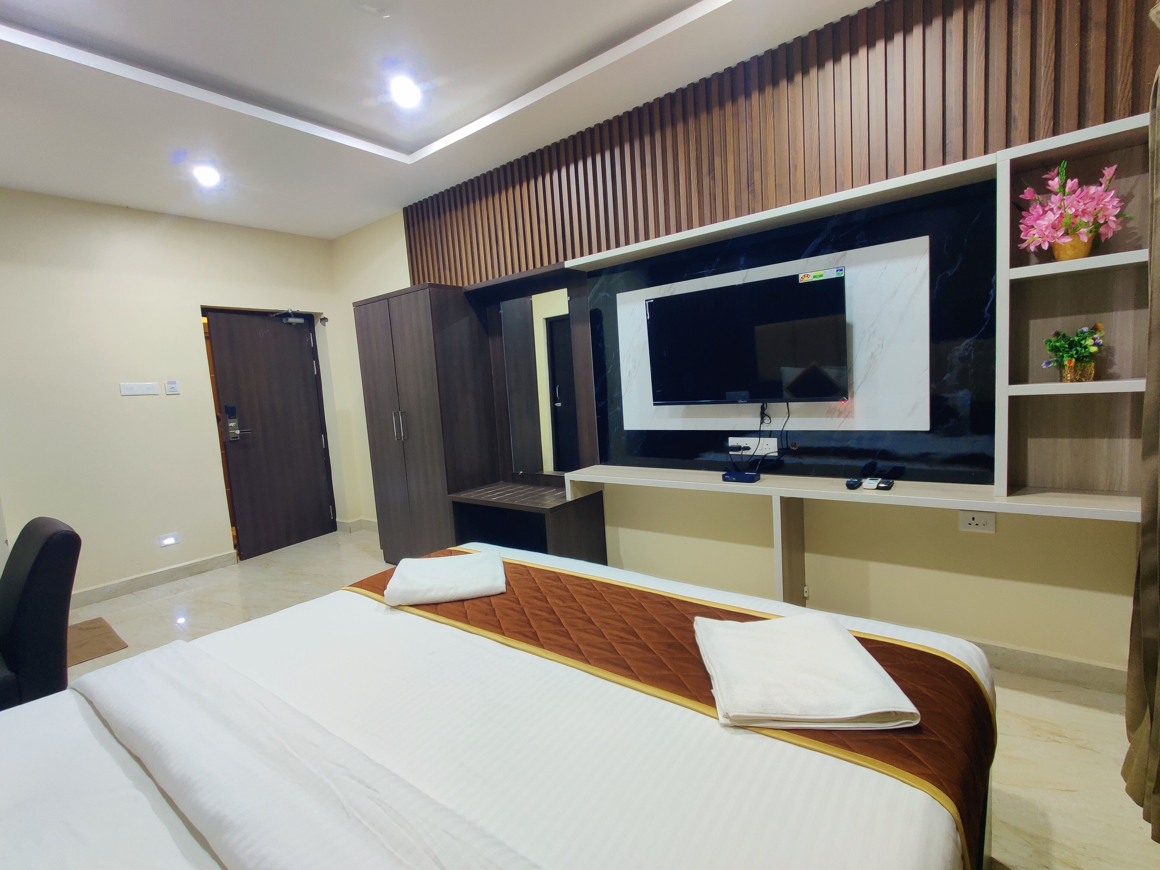 A hotel room with a bed, a TV, a wardrobe, and a desk with a computer.