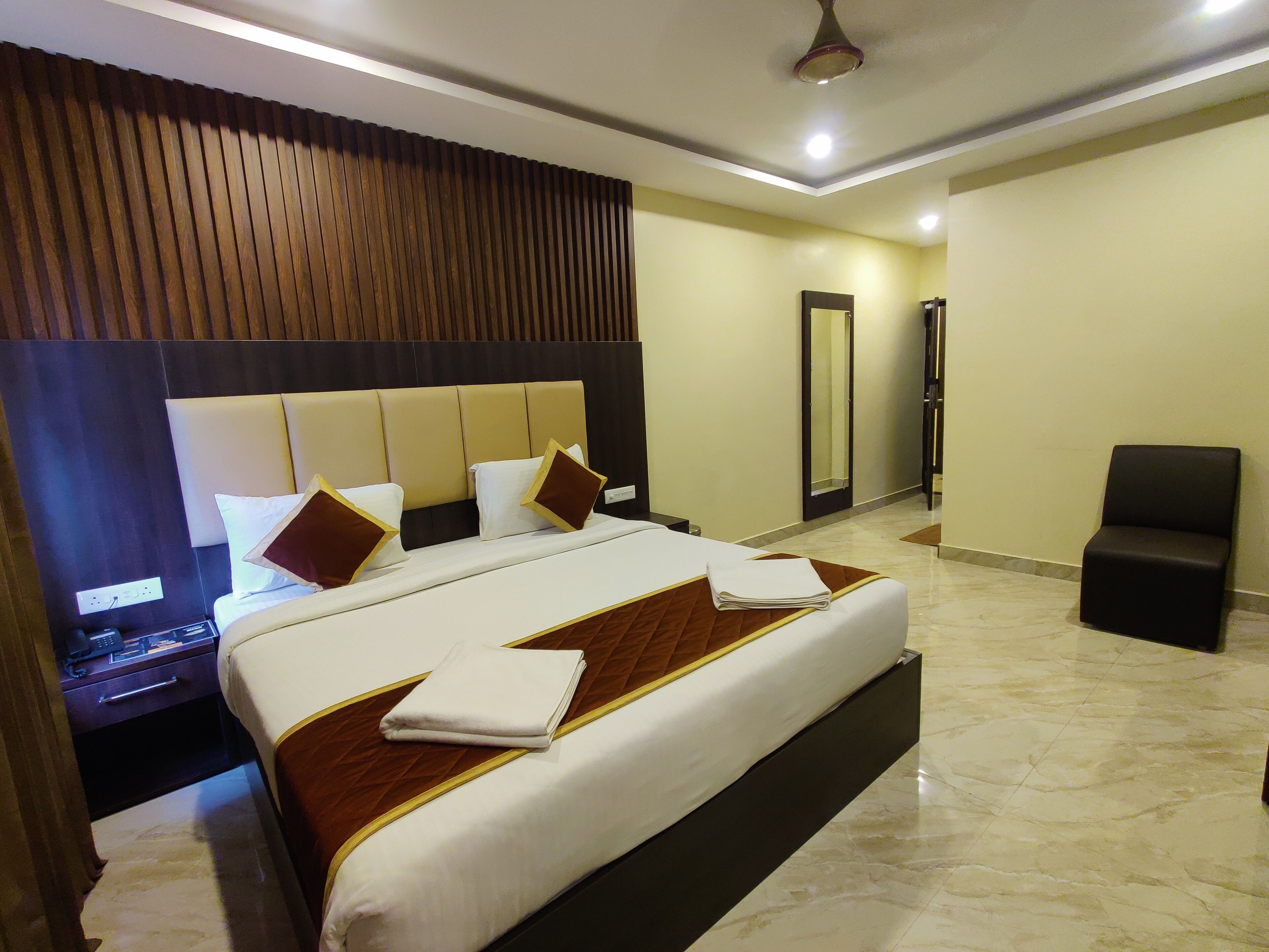 A hotel room with a large bed, a bedside table, a chair, and a mirror.