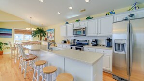 A modern kitchen with white cabinets, stainless steel appliances, and wooden bar stools. - 2 Blocks to Shore: Atlantic Beach Home w/ Views! (Atlantic Beach)