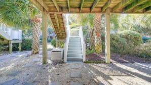 A covered outdoor area with a wooden staircase leading to a white door, surrounded by palm trees and a gravel path. - 2 Blocks to Shore: Atlantic Beach Home w/ Views! (Atlantic Beach)