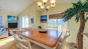 A dining area with a wooden table, white chairs, a chandelier, and a large plant. - 2 Blocks to Shore: Atlantic Beach Home w/ Views! (Atlantic Beach)
