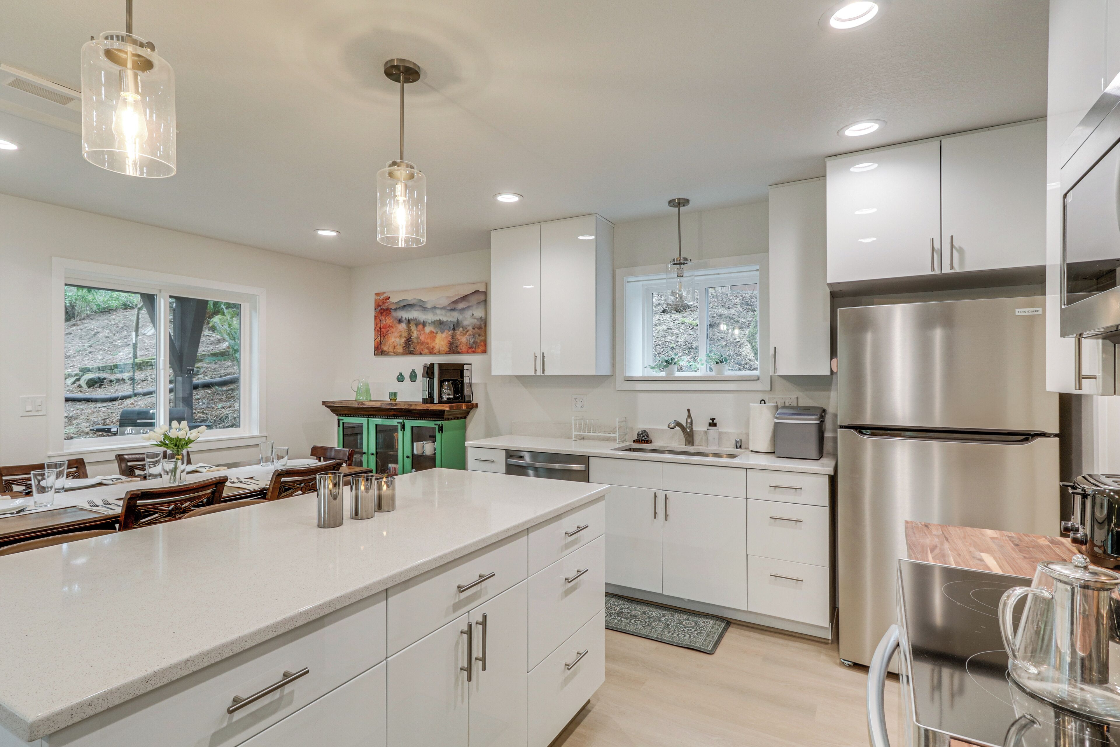 A modern kitchen with white cabinetry, stainless steel appliances, and pendant lighting.