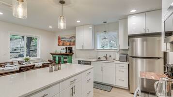 A modern kitchen with white cabinetry, stainless steel appliances, and pendant lighting.