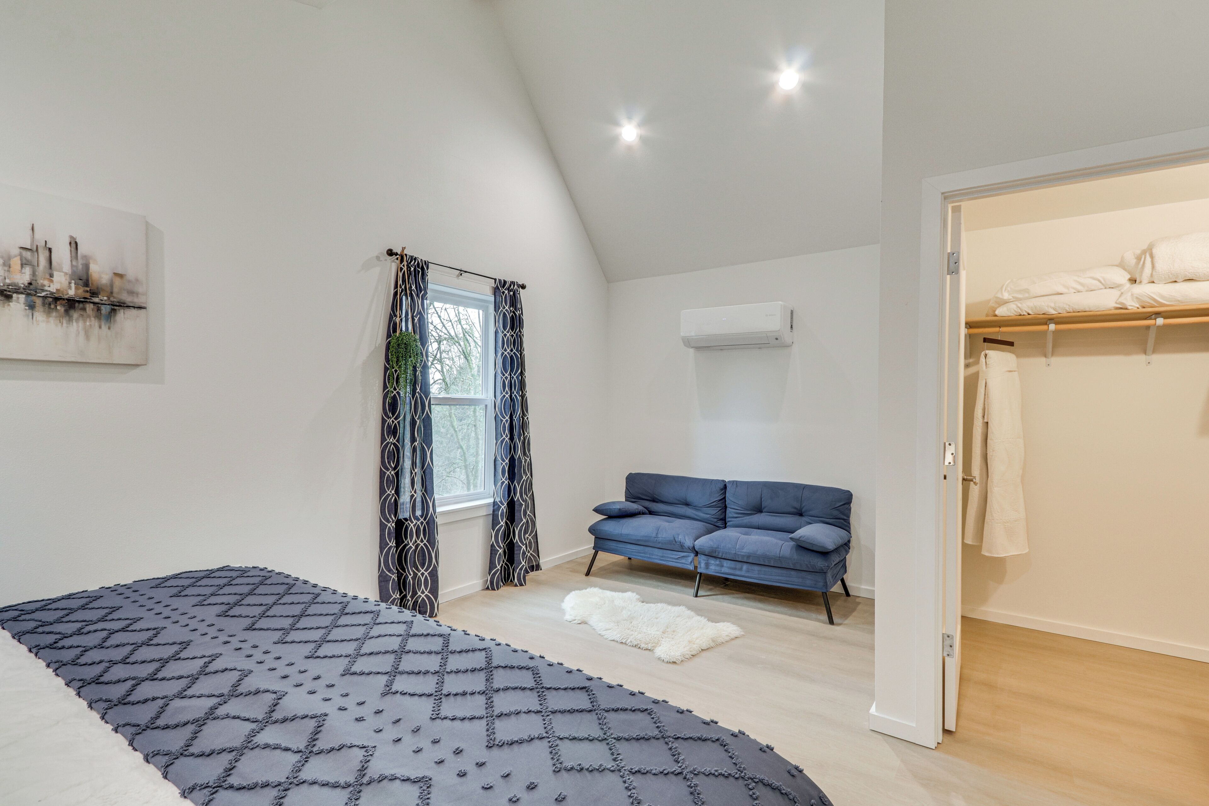 A modern bedroom with a bed, a blue sofa, a white rug, and a window with patterned curtains.