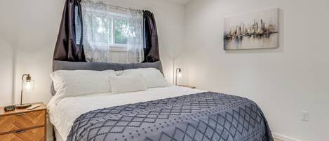 Ein Schlafzimmer mit Bett, Nachttischen, einem Fenster mit Vorhängen und einem Stadtbild an der Wand.