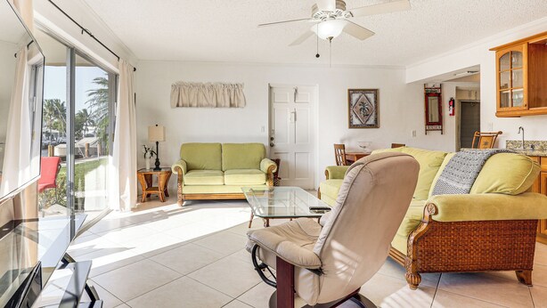 A spacious living room with a glass coffee table, a green sofa, a beige armchair, and a wicker sofa. - Waterfront Condo w/ Dock in Fort Lauderdale! (Fort Lauderdale)