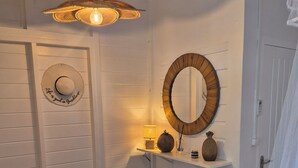 A hallway with a white door, a round mirror, a shelf with decorative items, and a hanging light fixture. - Villa Cannelle Pointe Batterie, sea view, pool, 3 bedrooms (DESHAIES)