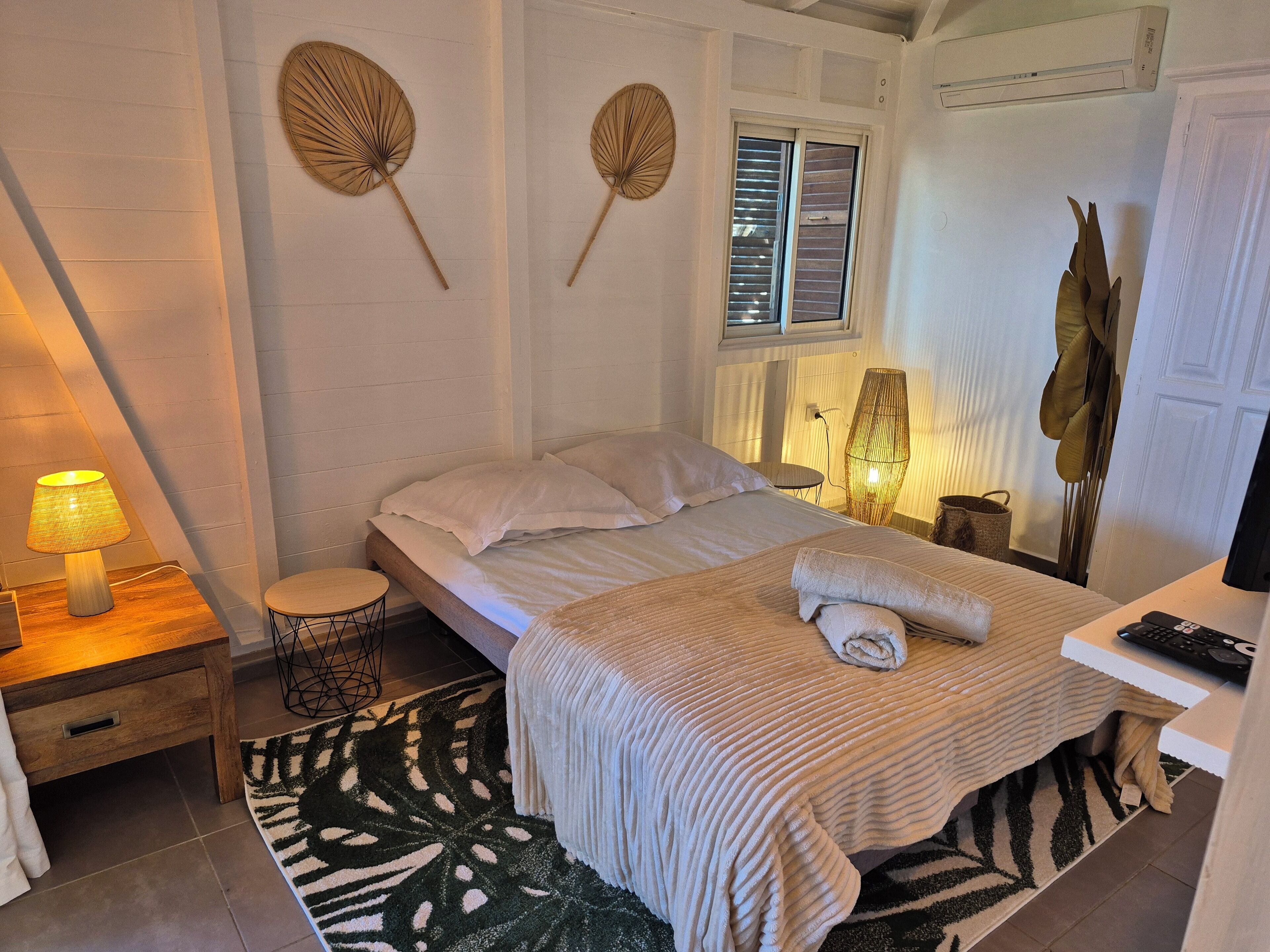 A bedroom with a bed, bedside table, lamp, and a large window.