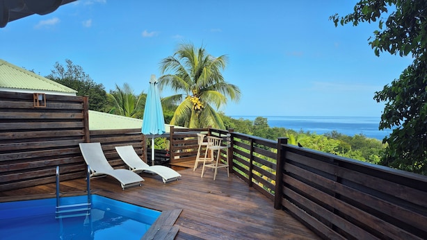 A wooden deck with a pool, lounge chairs, and a view of the ocean. - Villa Cannelle Pointe Batterie, sea view, pool, 3 bedrooms (DESHAIES)
