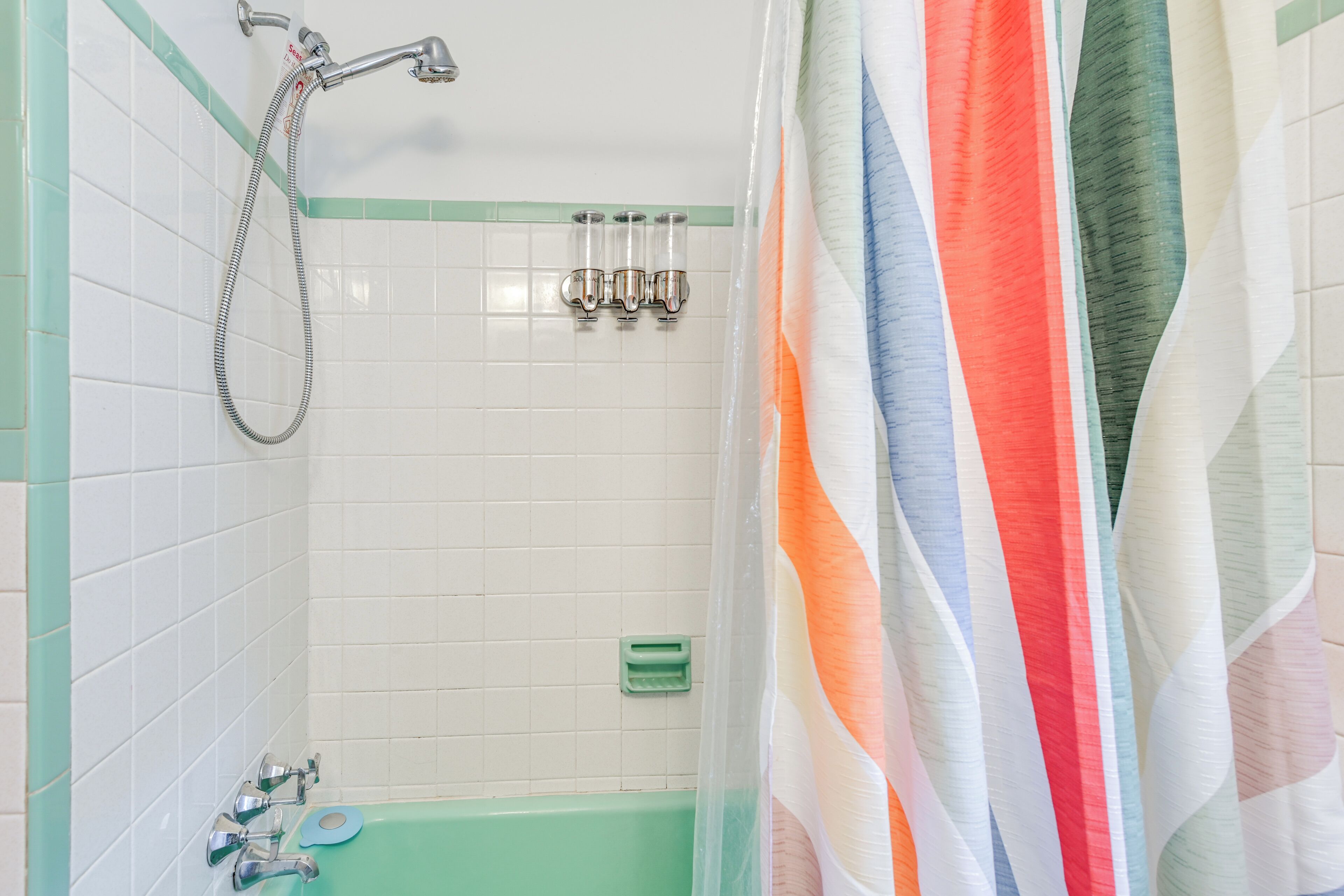 A bathroom with a green bathtub, a shower with a handheld hose, and a striped shower curtain.