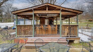Un gazebo de madera con techo cubierto, sillas y mesas de metal.