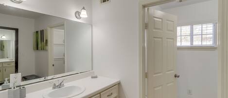 A bathroom with a white sink, a large mirror, and a door leading to another room.