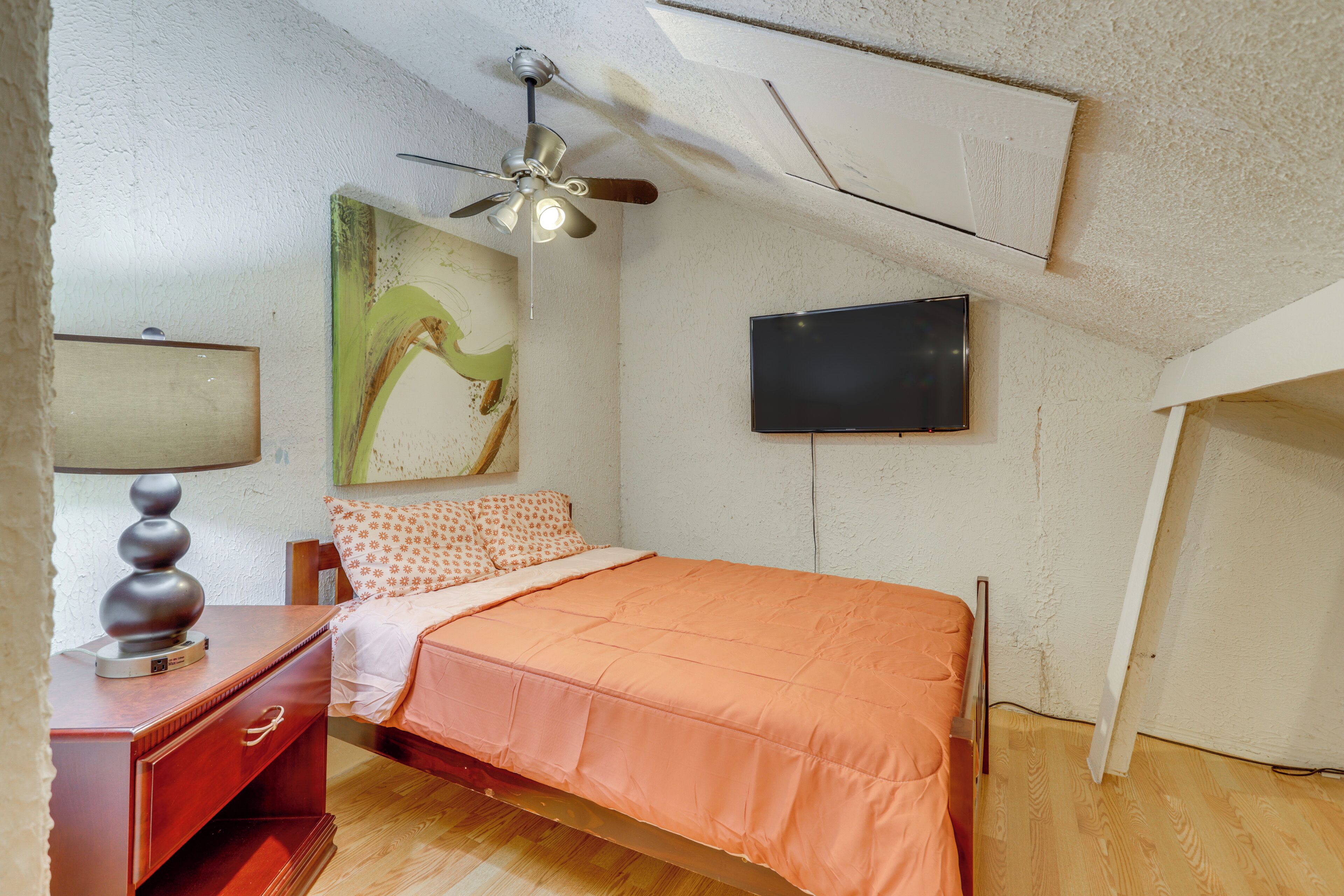 Ein Schlafzimmer mit einem Bett, einem Deckenventilator, einem Flachbildfernseher und einem Gemälde an der Wand.