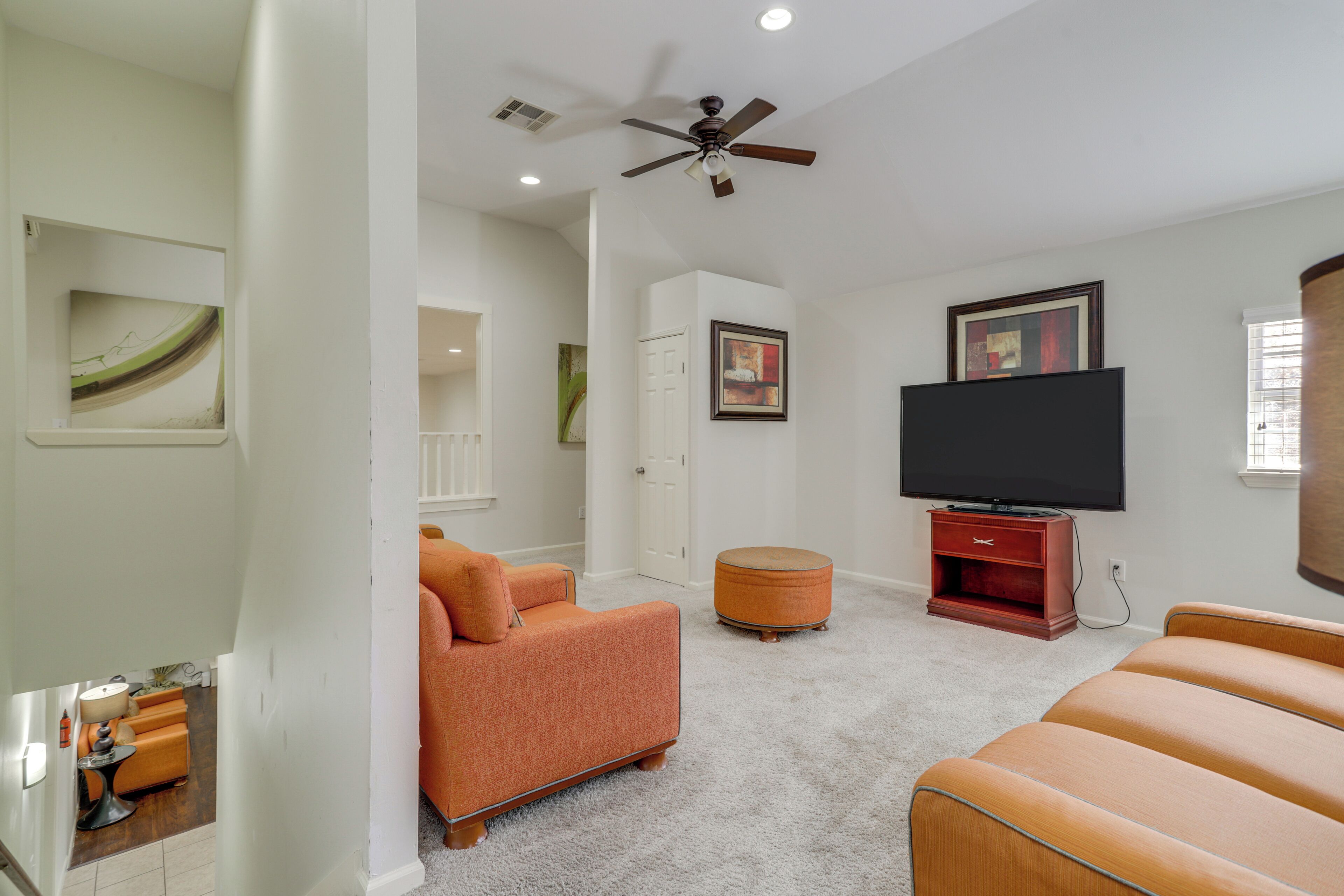 A living room with a ceiling fan, a flat-screen TV, and two orange sofas.