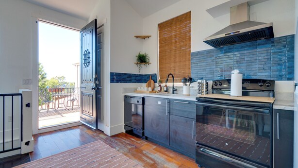 Una cocina moderna con horno grande, lavavajillas y puerta corrediza de vidrio a un balcón.