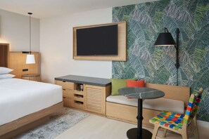 Habitación de hotel con cama, escritorio, silla, televisor y pared con diseño de hojas.