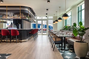 Un espace bar moderne avec un comptoir incurvé, des tabourets de bar rouges et un coin salon avec des tables et des chaises.