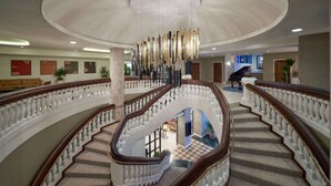 Una imponente escalera con un candelabro, un piano y un suelo de cuadros.