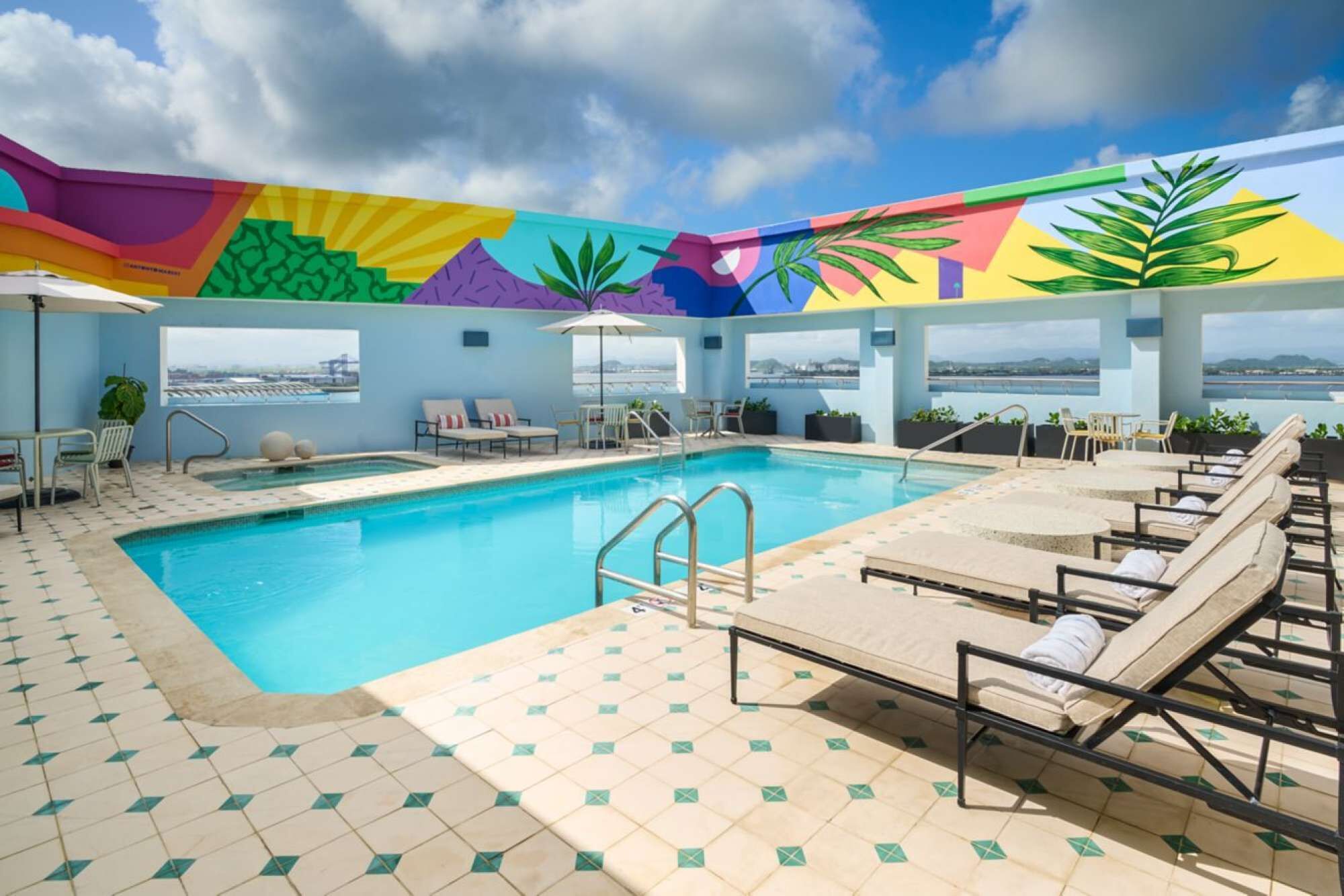 A rooftop pool area with lounge chairs, a pool, and a colorful mural.