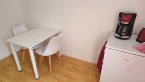 Une petite cuisine équipée avec une table et des chaises blanches, une machine à café et une bouilloire rouge posée sur un appareil blanc.