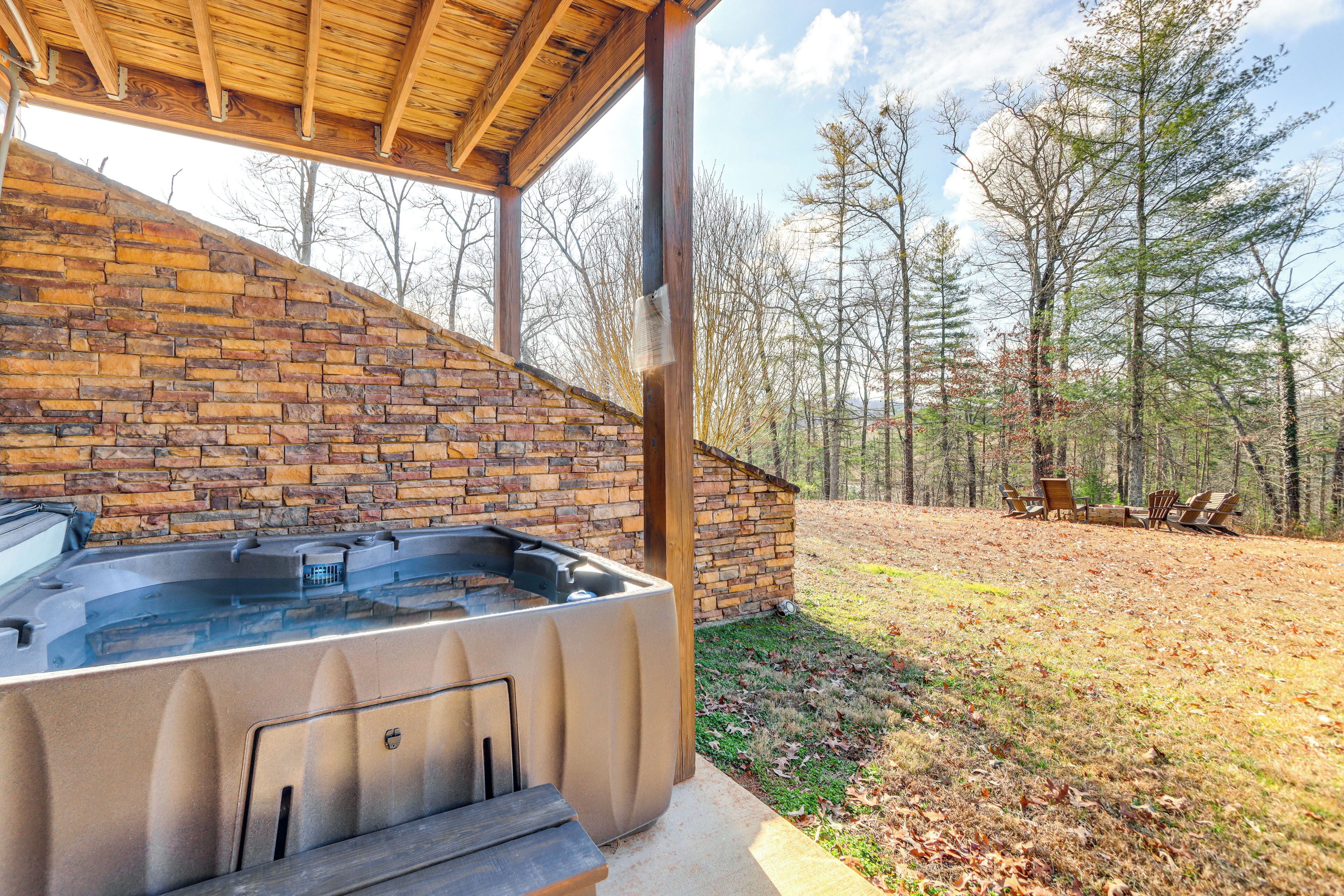 A hot tub under a wooden pergola with a brick wall, surrounded by a grassy area and trees.