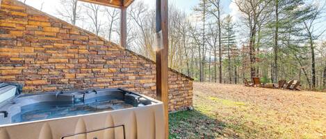 A hot tub under a wooden pergola with a brick wall, surrounded by a grassy area and trees.