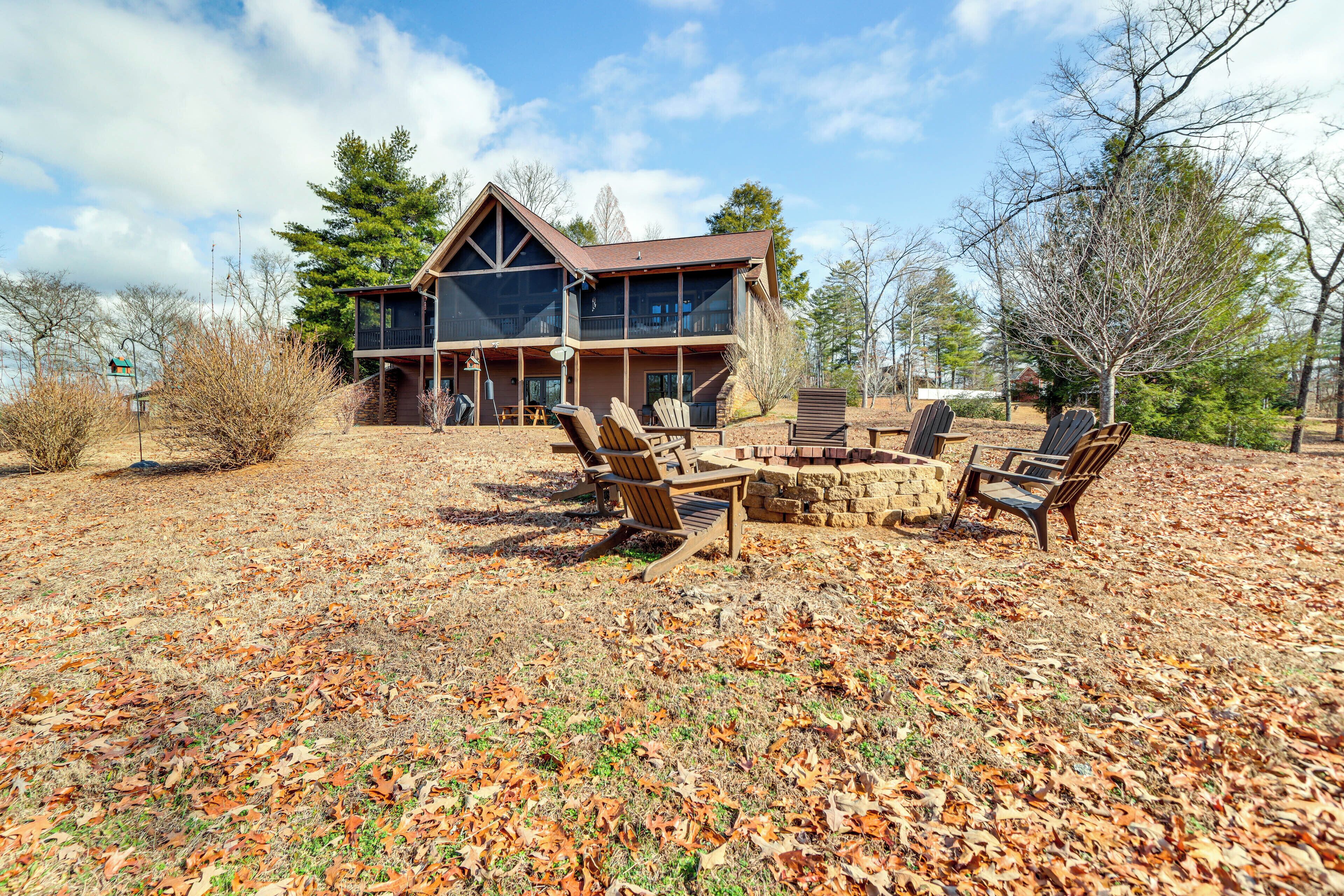 A two-story house with a stone fireplace, outdoor seating, and a large window overlooking a wooded area.