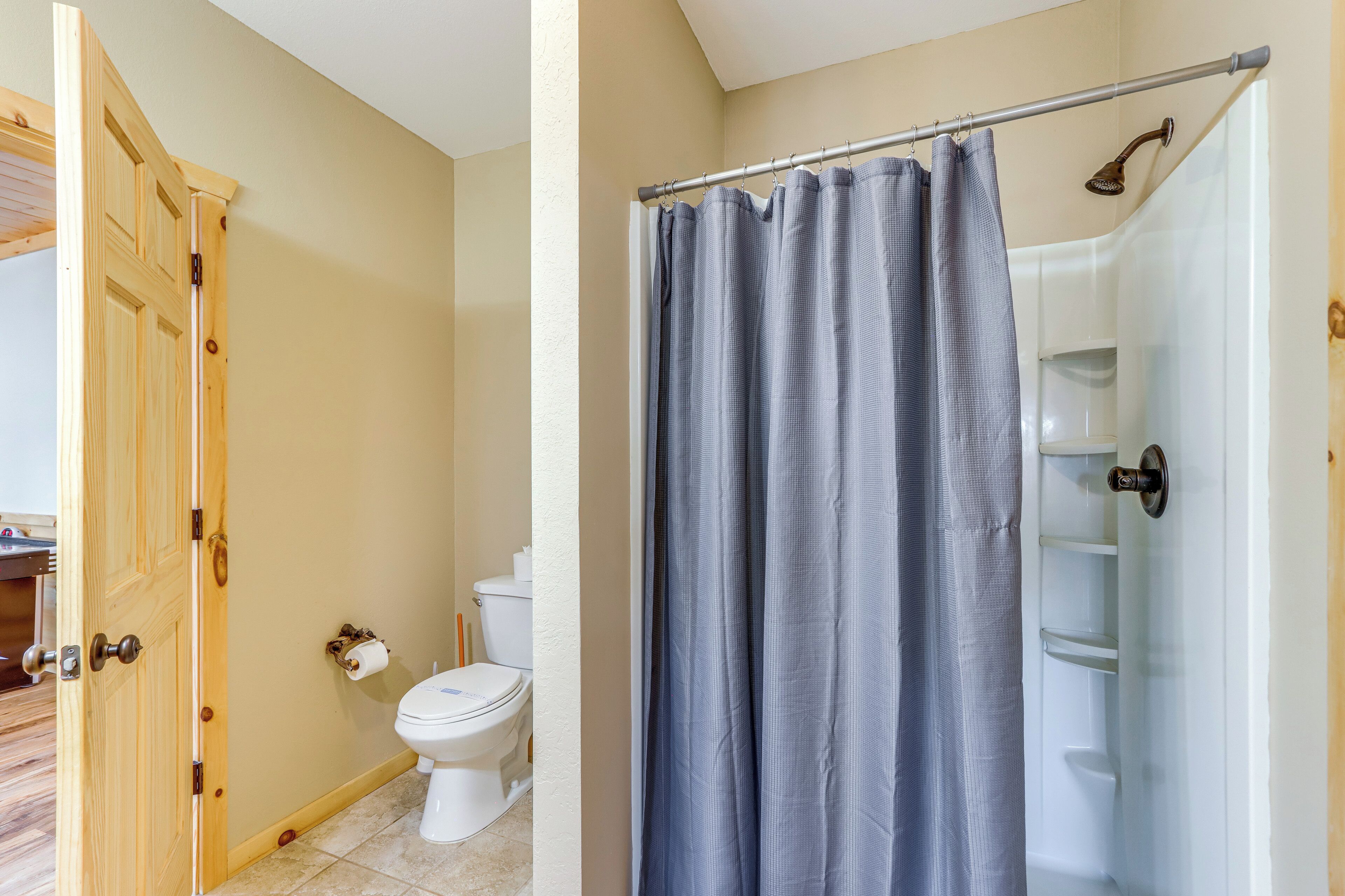 A bathroom with a toilet, a shower curtain, and a wooden door.