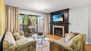 Ein Wohnzimmer mit floralen Sofas, einem Glastisch, einem Kamin und einem darüber montierten Fernseher.