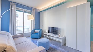 Un salon moderne avec un canapé, un pouf, une télévision et un fauteuil bleu.