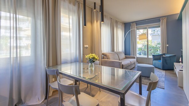Un salon moderne avec une table à manger en verre, des canapés gris et un fauteuil bleu.
