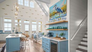 A spacious kitchen with a large island, a dining area with a blue sofa, and a staircase. - New home in CS South with access to 20+ resort like amenities (Port Aransas)