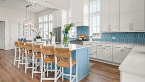 A spacious kitchen with white cabinetry, a blue backsplash, and a central island with bar stools. - New home in CS South with access to 20+ resort like amenities (Port Aransas)
