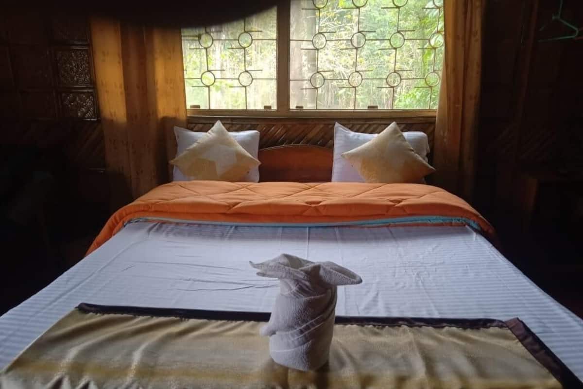 A bed with an orange bedspread, white pillows, and a towel on the bed.