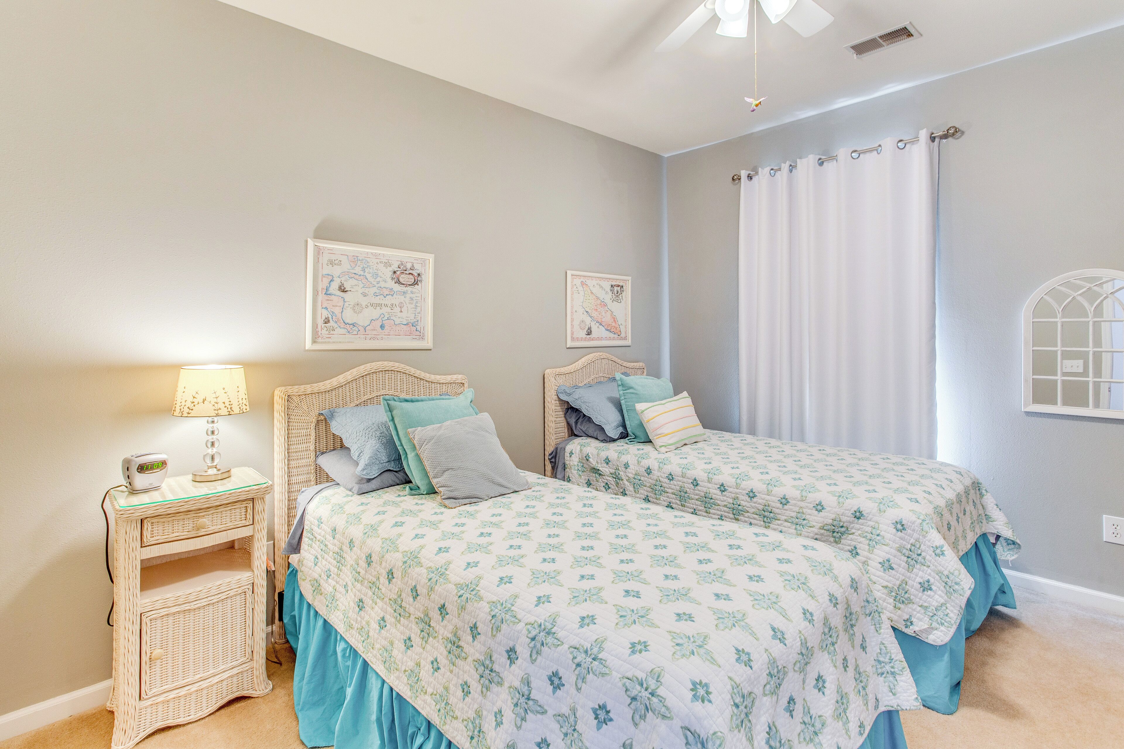 A bedroom with two beds, a nightstand, a lamp, and a window with curtains.