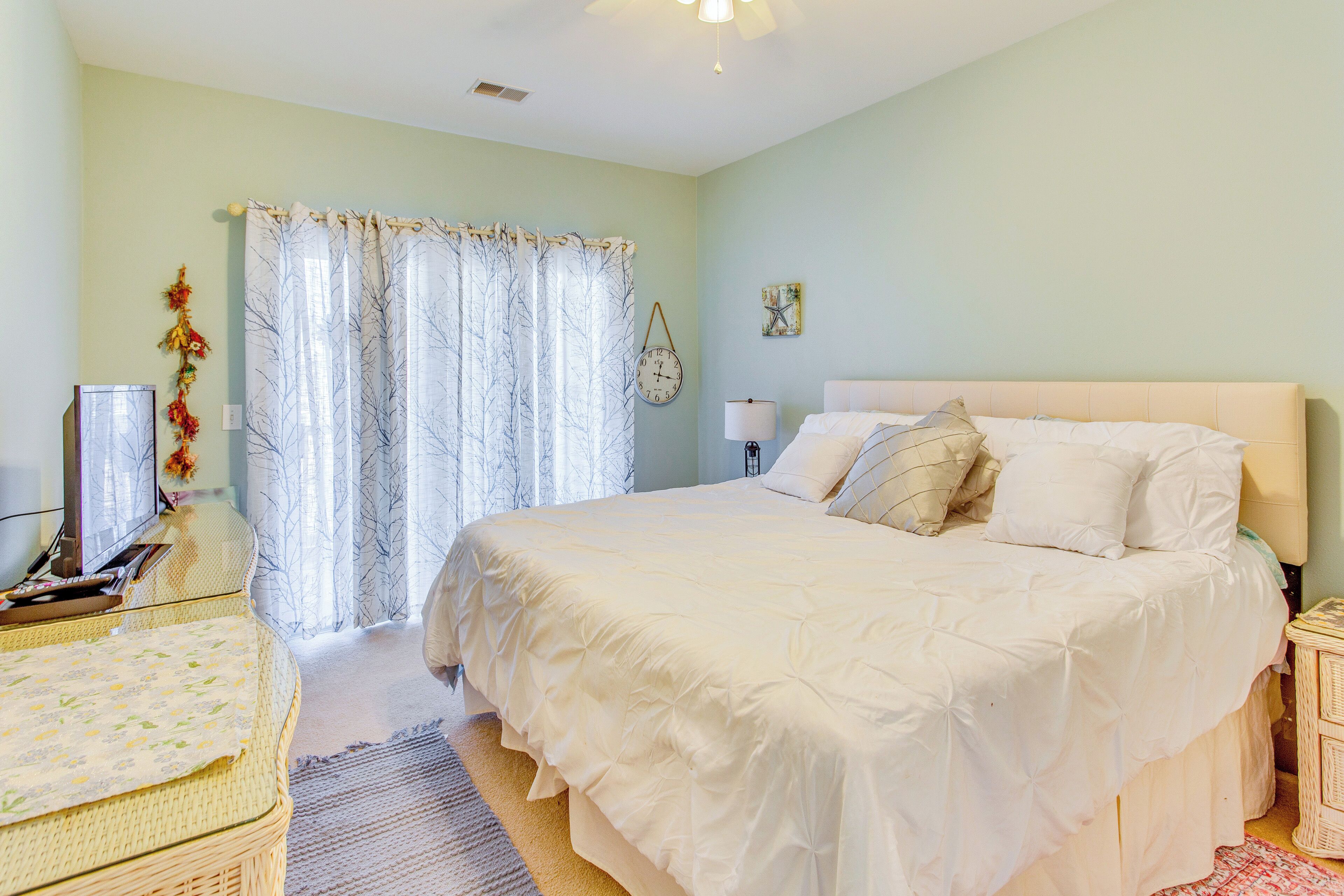 A bedroom with a large bed, a desk with a computer, a chair, a lamp, and a window with curtains.