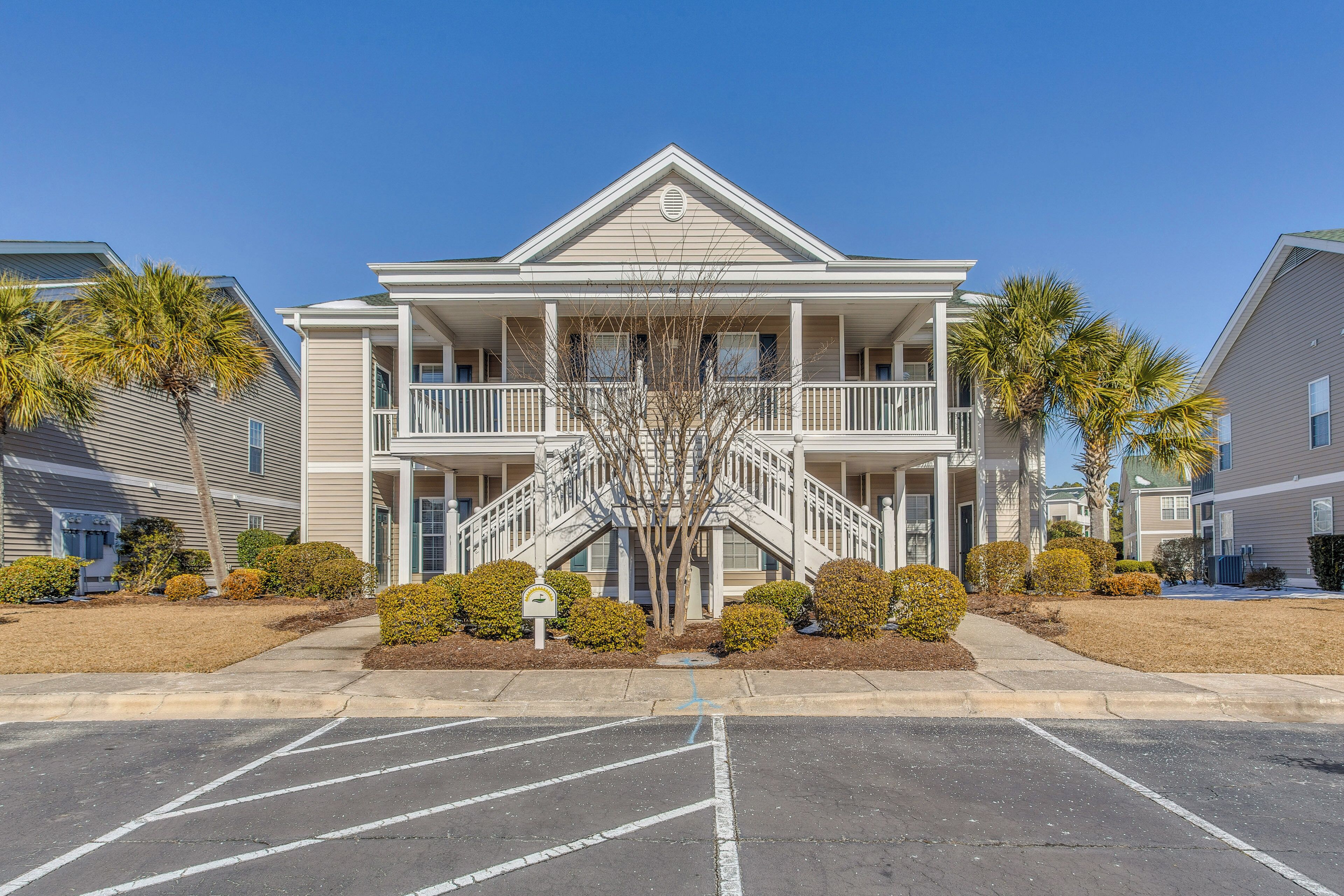Ein zweistöckiges Gebäude mit einer zentralen Treppe, Balkonen und einem Parkplatz davor.