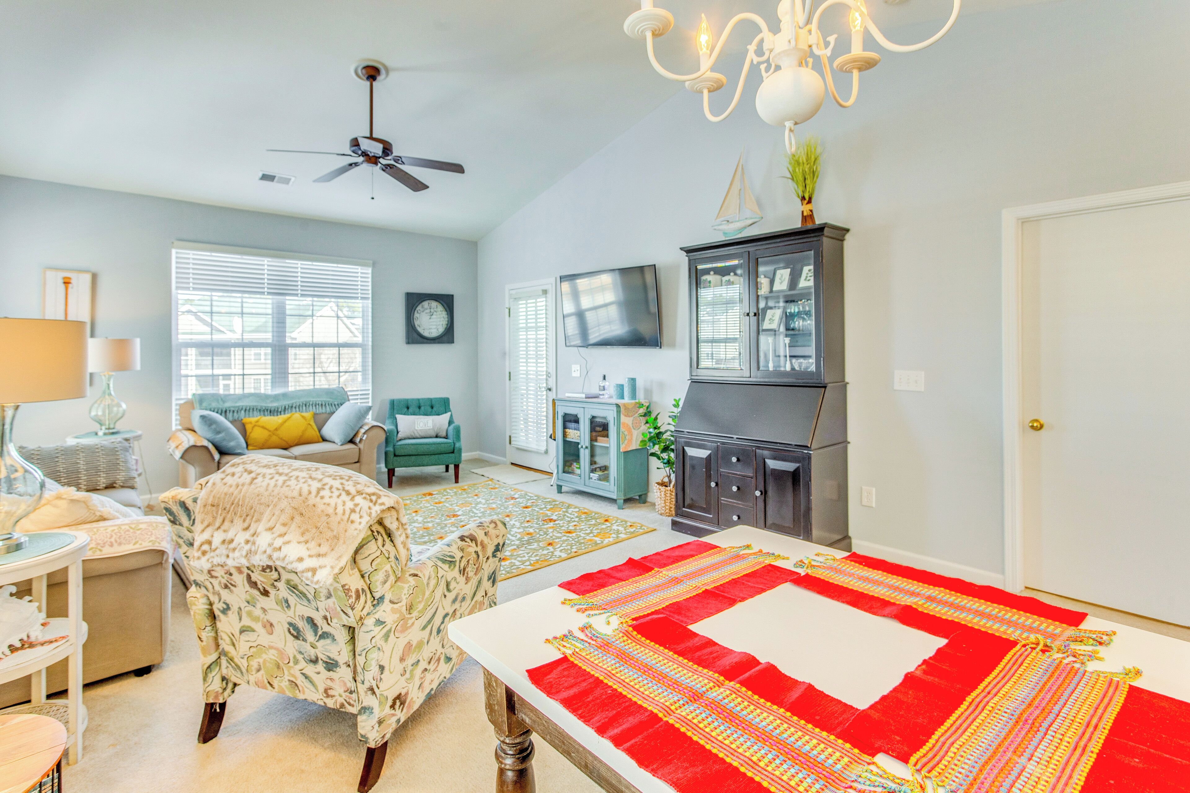 A spacious living room with a high ceiling, a ceiling fan, a fireplace, a television, and a dining area with a red and white table runner.