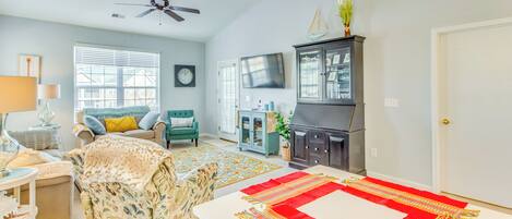 A spacious living room with a high ceiling, a ceiling fan, a fireplace, a television, and a dining area with a red and white table runner.