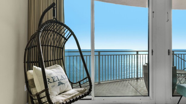 A balcony with a wicker chair and a view of the ocean. - Gulf-Front Bliss | Unique 2BR at Aqua Resort PCB (Panama City beach)