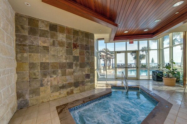 A spa area with a hot tub, stone walls, and a view of the pool and beach.