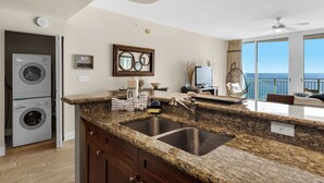 A kitchen with granite countertops, a double sink, and a built-in washer and dryer. - Gulf-Front Bliss | Unique 2BR at Aqua Resort PCB (Panama City beach)