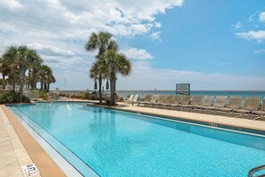 A pool with clear blue water, surrounded by lounge chairs and palm trees, with a view of the ocean and a 'No Diving' sign.