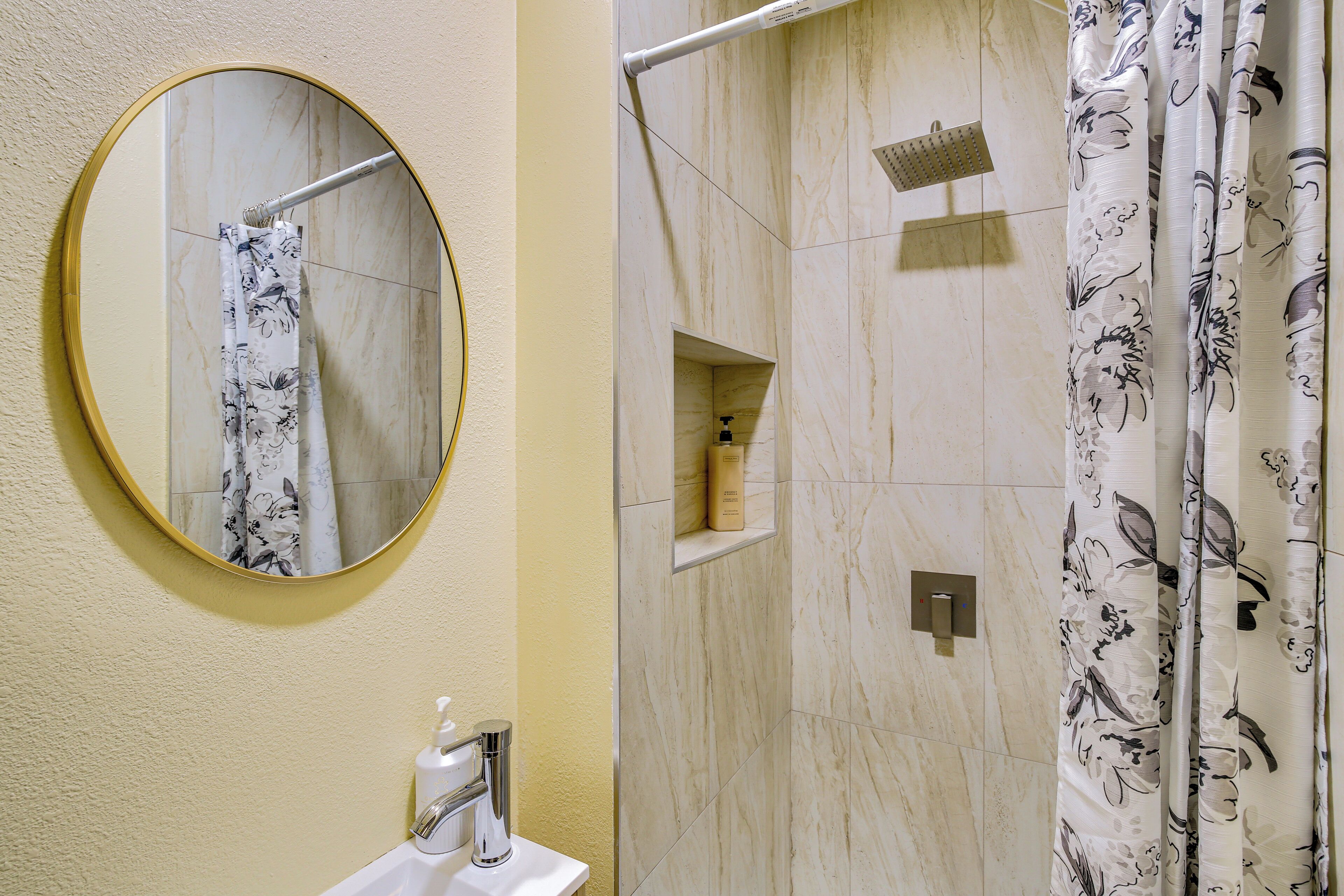 A bathroom with a round mirror, a sink, a shower with a glass enclosure, and floral shower curtains.