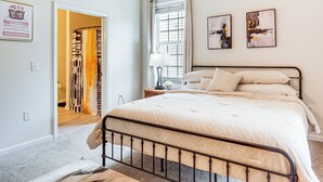 A bedroom with a large bed, a nightstand, a window with curtains, and a door leading to a hallway. - 9 Mi to Dtwn Fayetteville: Condo w/ Pool Access! (Fayetteville)