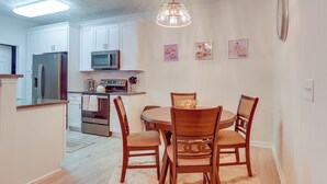 A modern kitchen with white cabinets, stainless steel appliances, and a dining area with wooden chairs and a glass bowl centerpiece. - 9 Mi to Dtwn Fayetteville: Condo w/ Pool Access! (Fayetteville)
